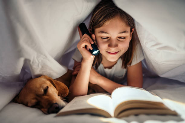 Fille qui lit dans son lit avec son petit chien sous une couette